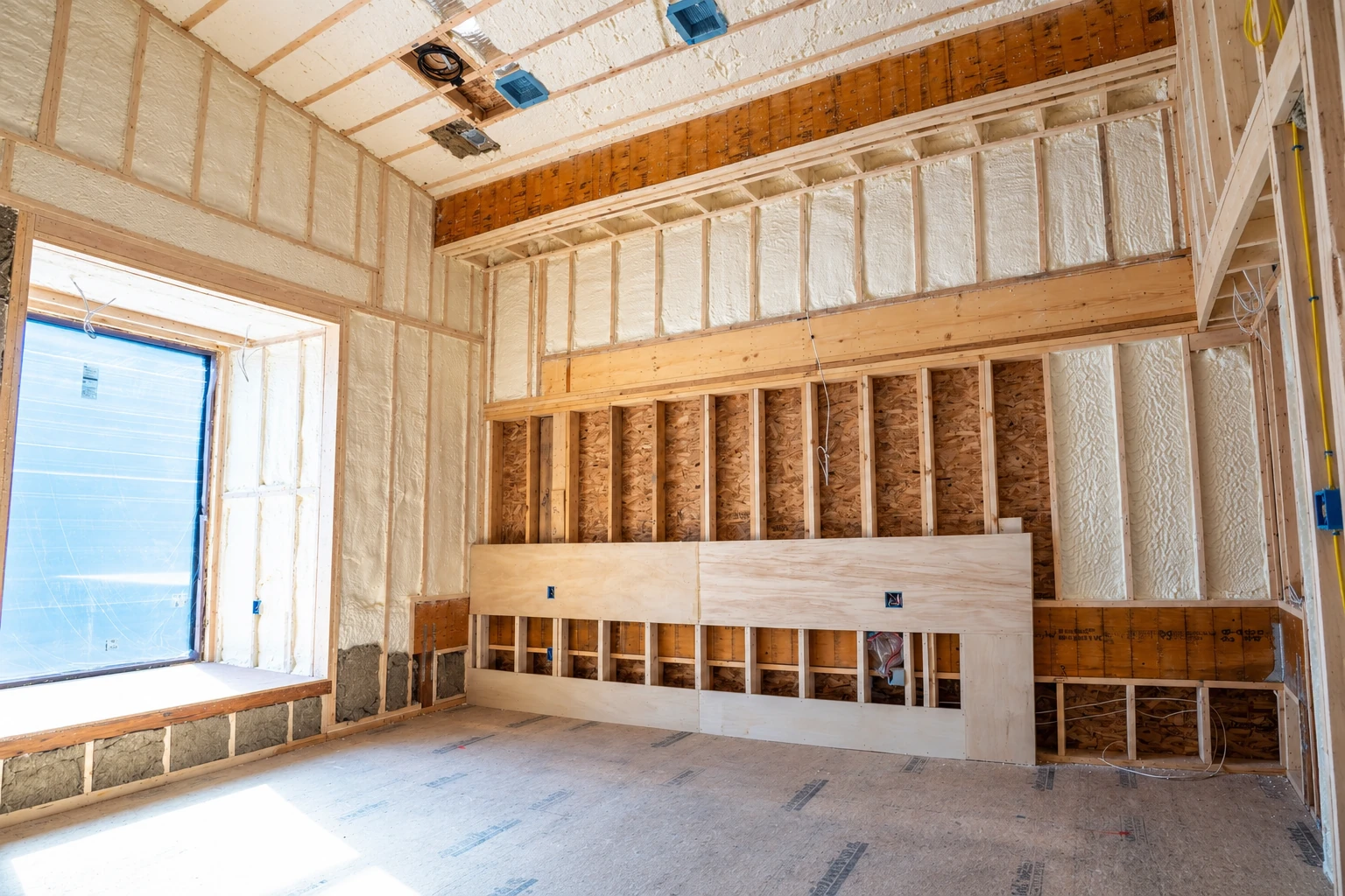 White spray foam fills wall and ceiling cavities in a partially framed room under construction.
