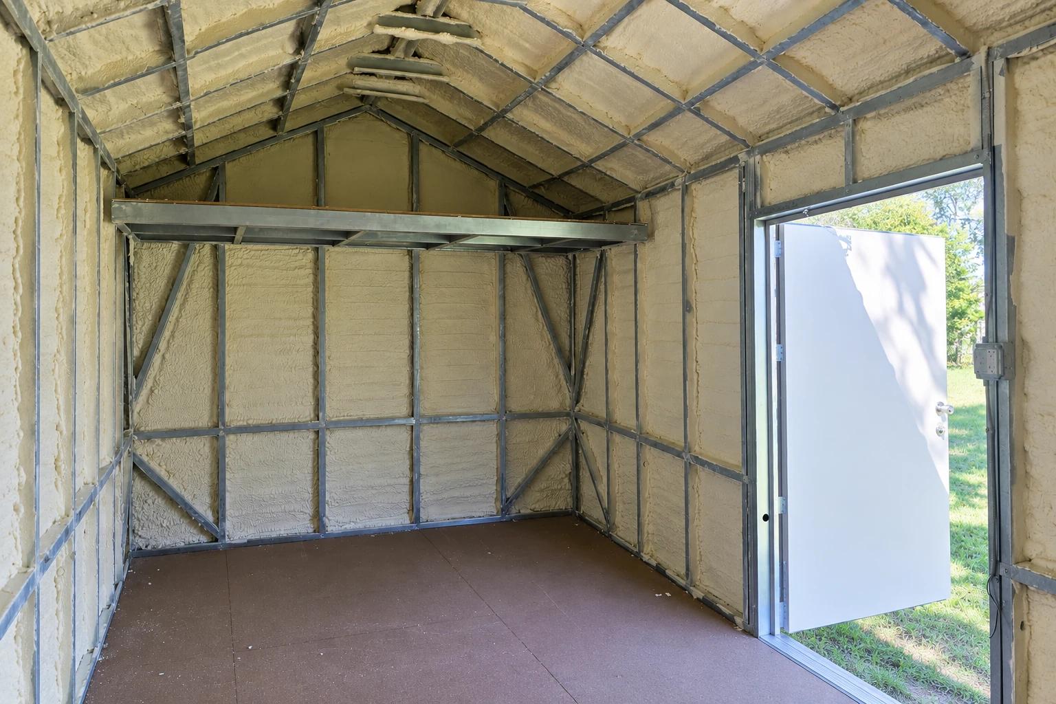 Commercial interior with cream spray foam covering the walls and pitched ceiling between exposed metal framing; an open door leads outside.